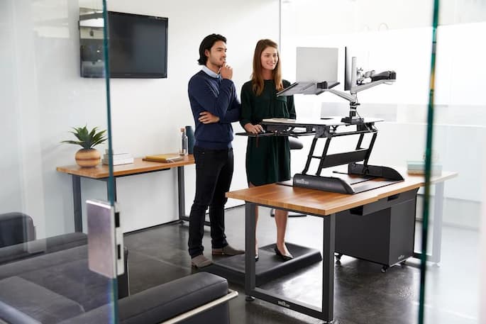 a man and a woman standing in front of the standing desk at the office